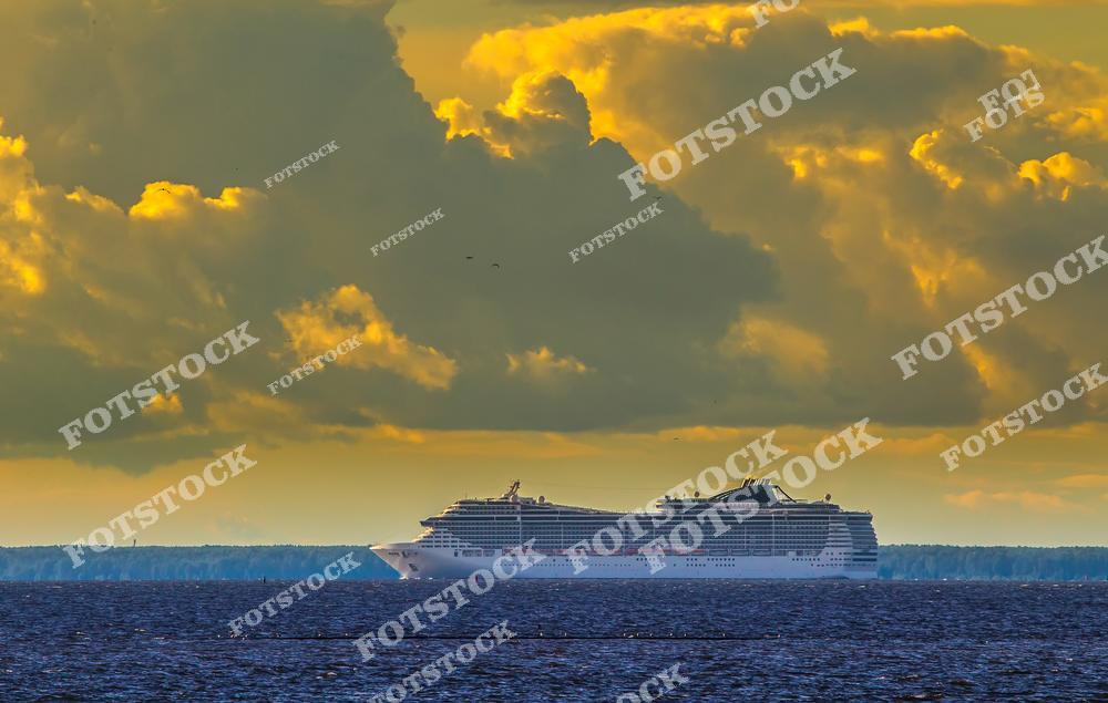 На фотографии изображен круизный лайнер, идущий по морю под драматичным небом, окрашенным закатным светом. Облака и мягкий свет создают атмосферу величия и спокойствия. Снимок символизирует мечты о путешествиях и красоту морских приключений.